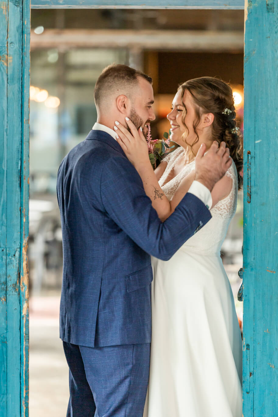 Bruid en bruidegom in een blauwe deuropening. Ze staan tegenover elkaar en houden elkaar liefdevol vast.